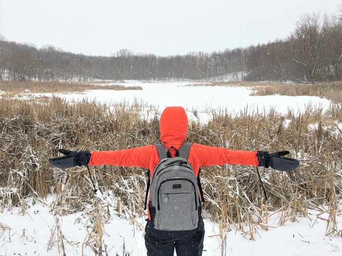 French Regional Park A woman wearing a red parka and a backpack stands by the edge of a frozen lake with arms outstretched
