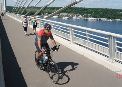 A man wearing a helmet rides his bicycle across a bridge