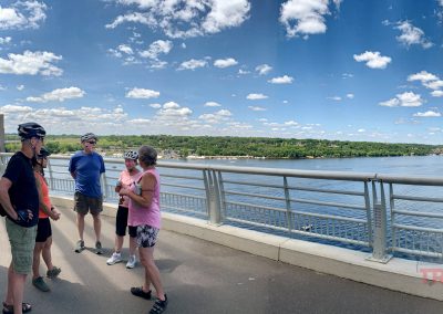 A group of men and women pause to take in the view of a river from a tall bridge