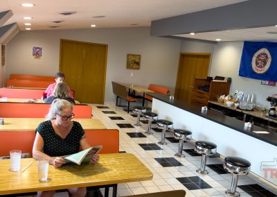 A woman reads the newspaper in a diner with formica booths, chrome swivel stools and black and white checker floors