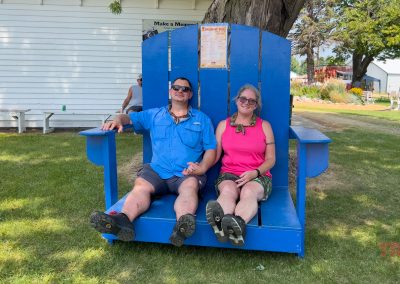 A man and a woman hold hands while seated in an oversized blue Adirondack chair