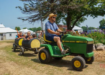A man pulls children in carts around a fair with a John Deere lawnmower