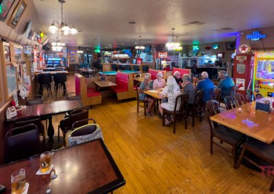 The interior of a bar with tables, booths and lots of neon signs