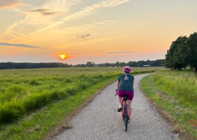 A woman rides her bike on a paved trail into the sunset
