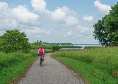 A woman rides her bike on a paved trail along a lake