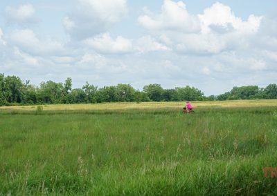 A woman rides her bike on a paved trail through a meadow
