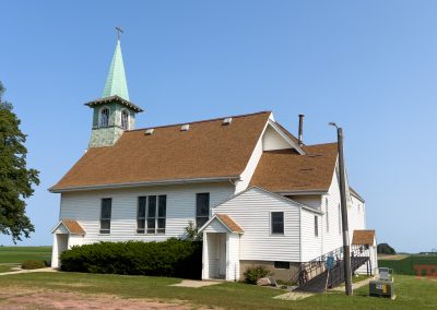 A white wood-clad church with a copper-colored steeple sits in a field