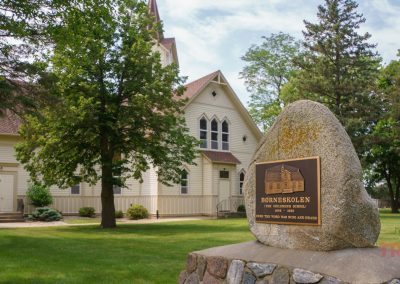 A rock in front of a church bears a plaque with the word 'Borneskolen' on it
