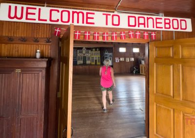 A woman walks into a room whose entrance bears a banner reading 'Welcome to Danebod' and Danish flags