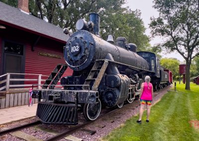 a woman looks at a historic steam engine on display in a park