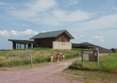 A woman and three children walk away from an interpretive center in a grassy field