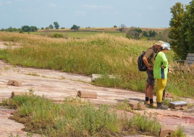 A man and two women study an interpretive sign while standing on a plateau of red rock