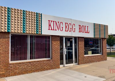 The outside of a small, red brick building bears a large sign with the words 'King Egg Roll'
