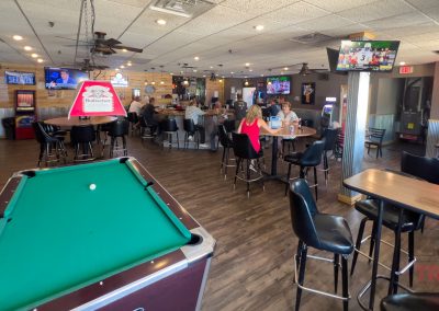 The interior of a bar with patrons seated at tables and a pool table