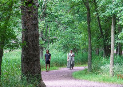A woman and a boy walk through the woods on a gravel path