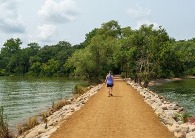A woman walks across a narrow land bridge in a lake to a wooded island