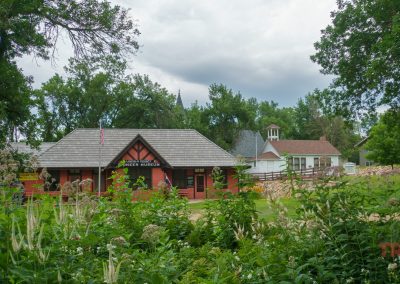 The exterior of the grounds of a museum with a red, wood clad train station and other historical buildings