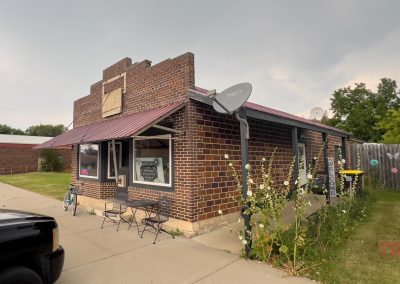 The brown brick exterior of a very small restaurant with a maroon awning