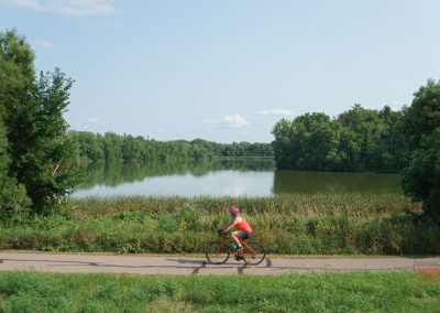 A woman rides her bike on a paved trail by a lake