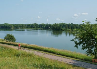 A woman rides her bike on a paved trail by a lake