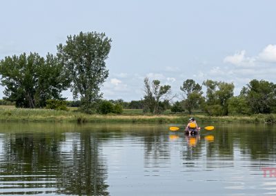 A woman floats on a tree lined lake in a kayak
