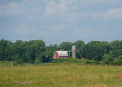 A landscape view of a red barn and cement silo across a prairie meadow