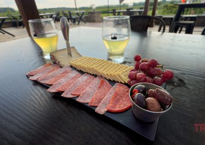 A closeup of two glasses of apple cider and a charcuterie board on an outdoor table