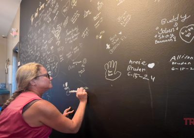 A woman signs a black message board with a white marker