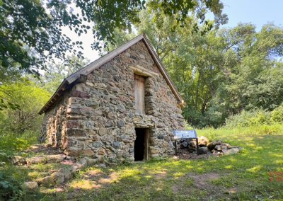 A small house made of field stone sits in a clearing of a forest