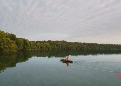 A woman paddles a kayak on a calm lake ringed by trees