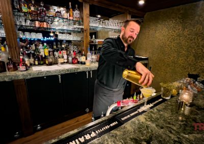 A male bartender pours a cocktail from a gold cocktail shaker