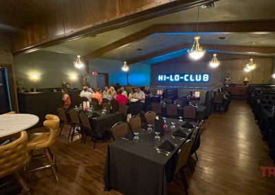 A dimly lit dining room features the HI-Lo-Club name in neon on the back wall