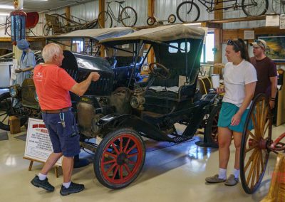 A man opens the hood to an antique car while a man and a woman look on