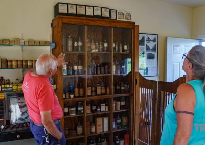 A man and a woman study the contents of an antique apothecary cabinet