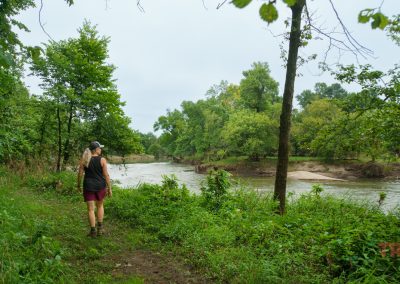 A woman walks along the forested banks of a river Kilen Woods State Park.