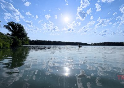 A person in a kayak paddle on a calm lake on a sunny day