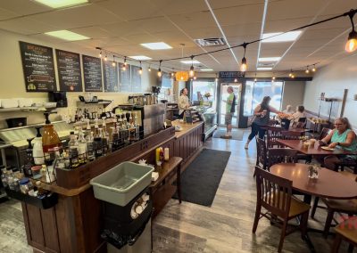 the interior of a coffee shop with patrons waiting to be served at a counter and seated at tables