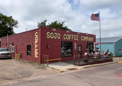 The outside of a reddish one-story brick building with a patio and an American flag on a pole