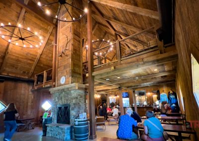 The wood-clad interior of a brewery with high ceilings and large wagon wheel chandeliers
