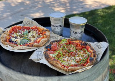 Closeup of two wood fired pizzas and two beers on a barrel
