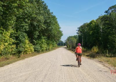 A woman on a bicycle rides along a gravel road