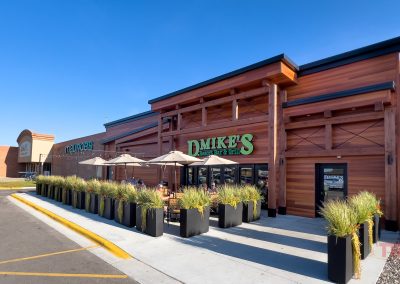 The patio outside of a restaurant clad in brown wood is lined with planters