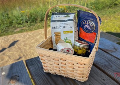 A basket filled with cheese, olives, salmon and crackers on a picnic table