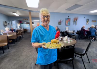 A server in a blue smock present a plate of breakfast food