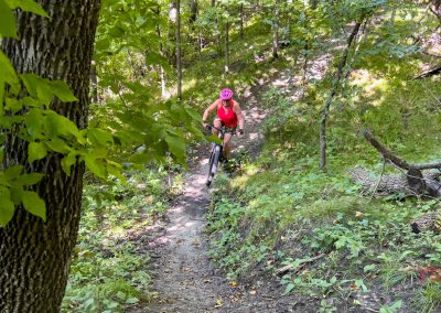 A woman rides a mountain bike through a forest at Kensington Rune Stone Park.