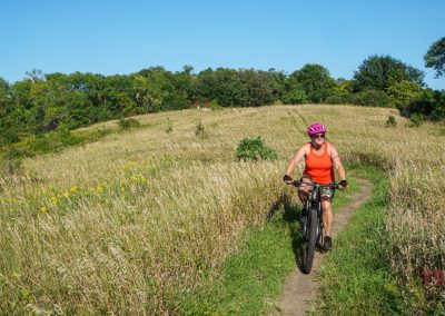 A woman rides a mountain bike through a grassy field at Kensington Rune Stone Park.