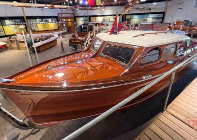 An antique fiberglass boat on display inside of a museum gleams with polished chrome and varnished mahogany