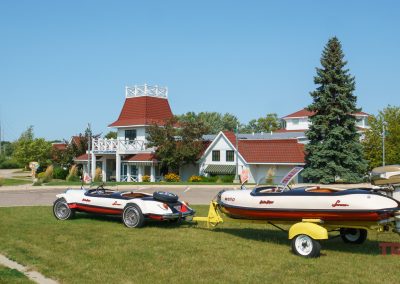 A unique matching boat and antique car are displayed outside of a museum