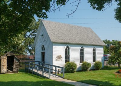 A small, white, wooden church on the grounds of a museum