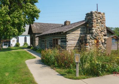 A log building with a stone fireplace on display on the grounds of a museum